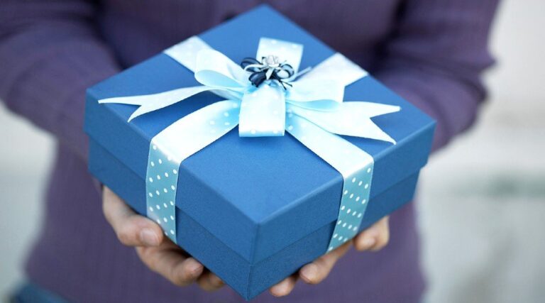 Embrulho de presente azul sendo entregue por mãos femininas||