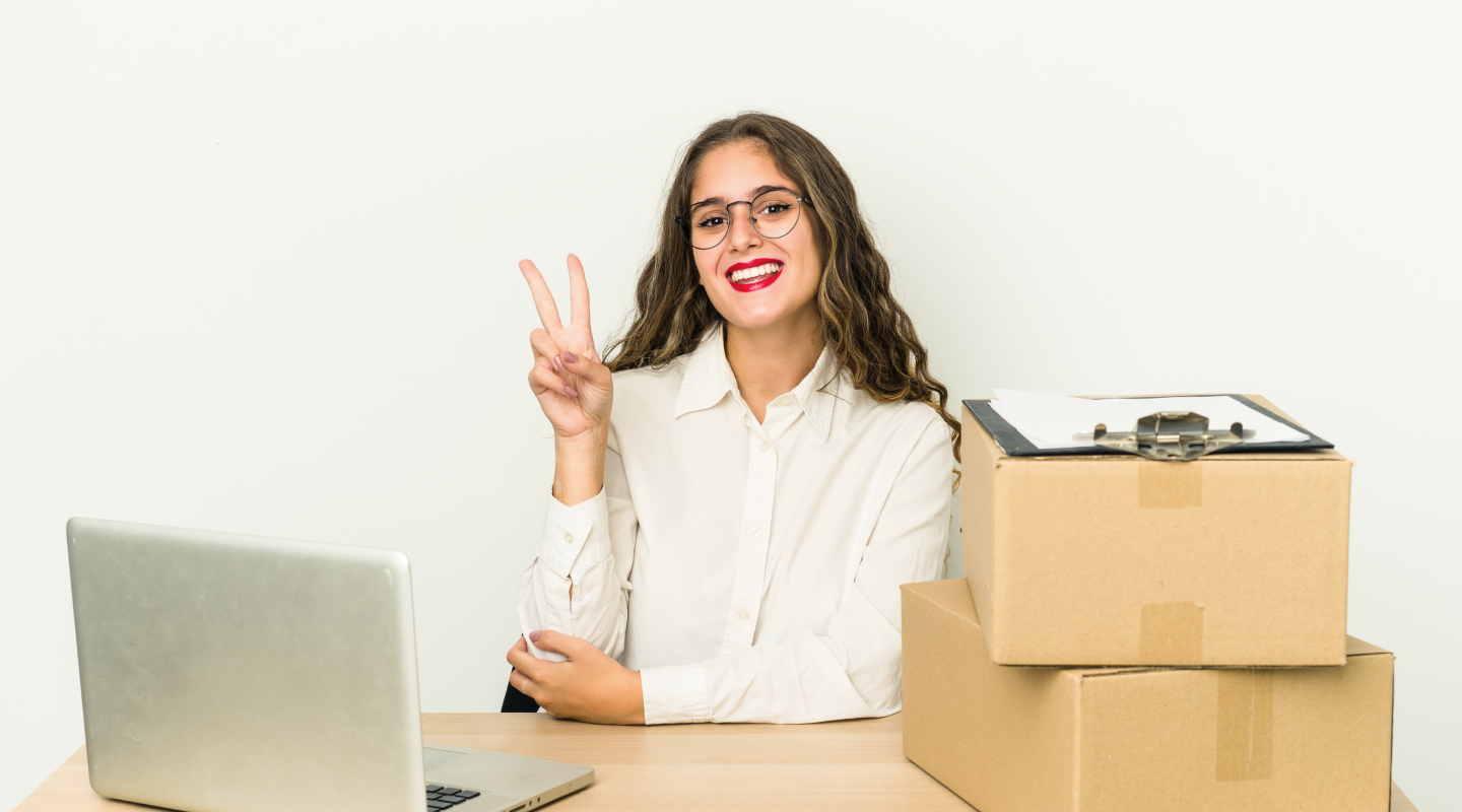 Mulher lojista feliz em seu escritório com um computador e caixas em cima de sua mesa